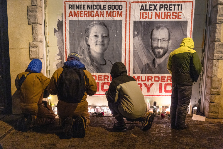 Four people stand in front of a candle-lit vigil at night.