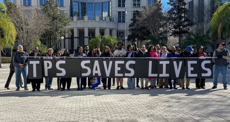 A group of people stands in front of the Orange County Courthouse while holding a sign that says "TPS Saves Lives".