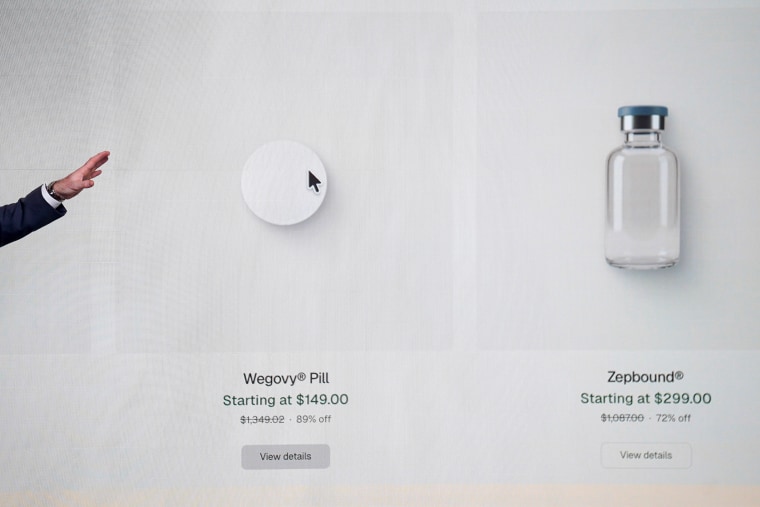 A hand gestures from outside the frame toward a digital display of a pill and medical vial that is projected on a white wall.