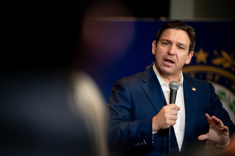 Ron DeSantis gestures with one hand while holding a microphone in his other hand during a campaign event.