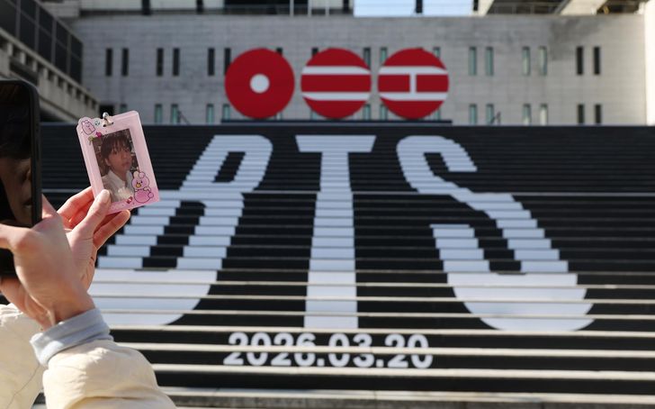 A visitor takes a picture of a photocard in front of a street installation promoting K-pop boy band BTS' comeback at Gwanghwamun Square in central Seoul, Jan. 22. Yonhap 