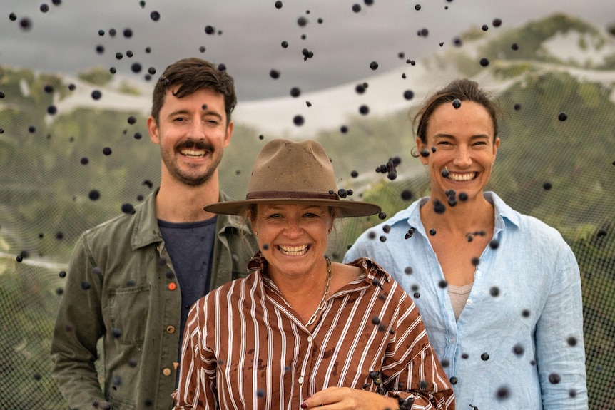A man and two women smile with grapes surrounding them in the air.