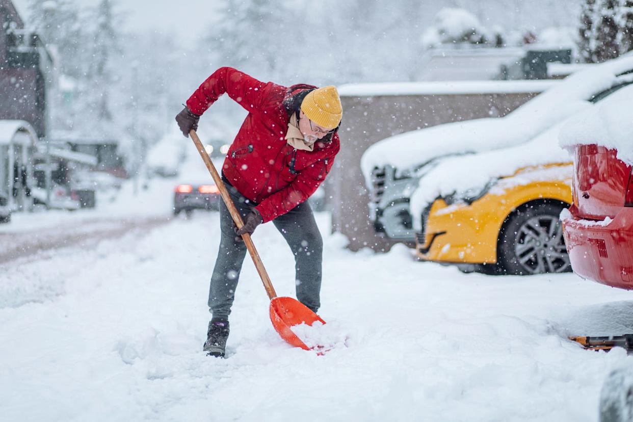 man in red jacket shoveling snow during a heavy snowfall in a residential area