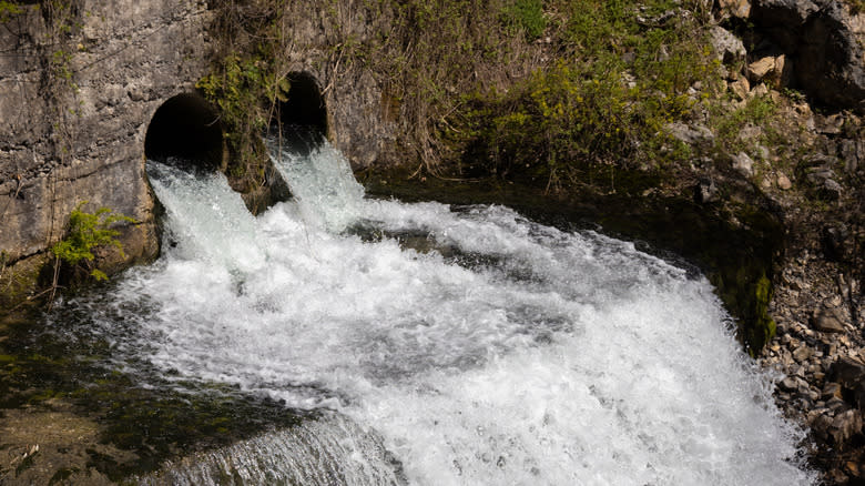 A stream of water flowing out of culverts under a road