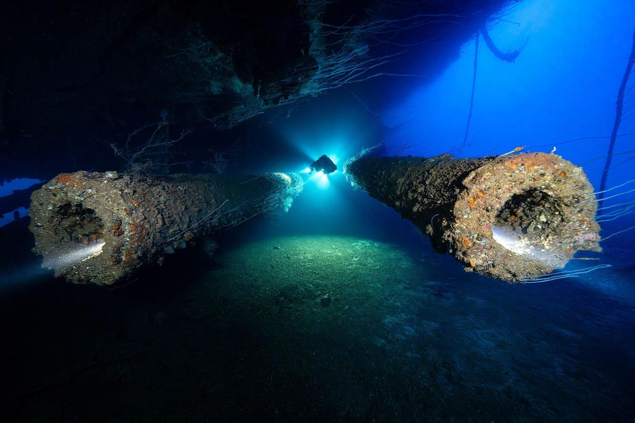 The wreck of Japanese battleship, IJN Nagato, in the Bikini Atoll. The picture shows a diver with a torch light swimming between the twin stern guns