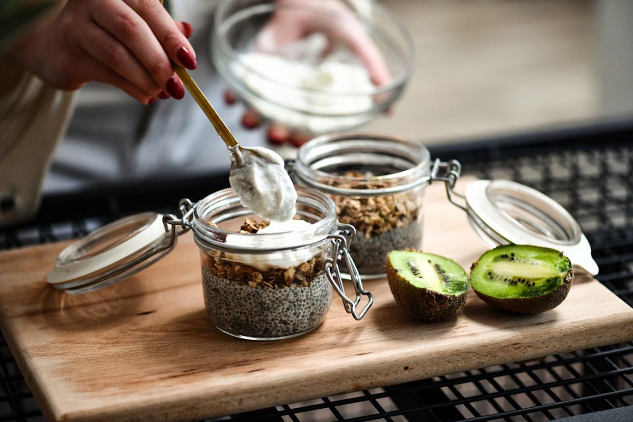 female preparing healthy breakfast jars adding yogurt to chia pudding with granola