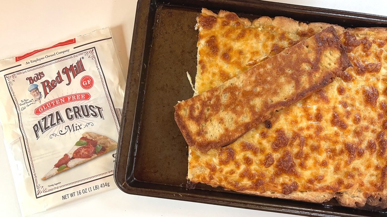 Bag of Bob's Red Mill Gluten Free pizza crust mix on table next to pizza on baking sheet