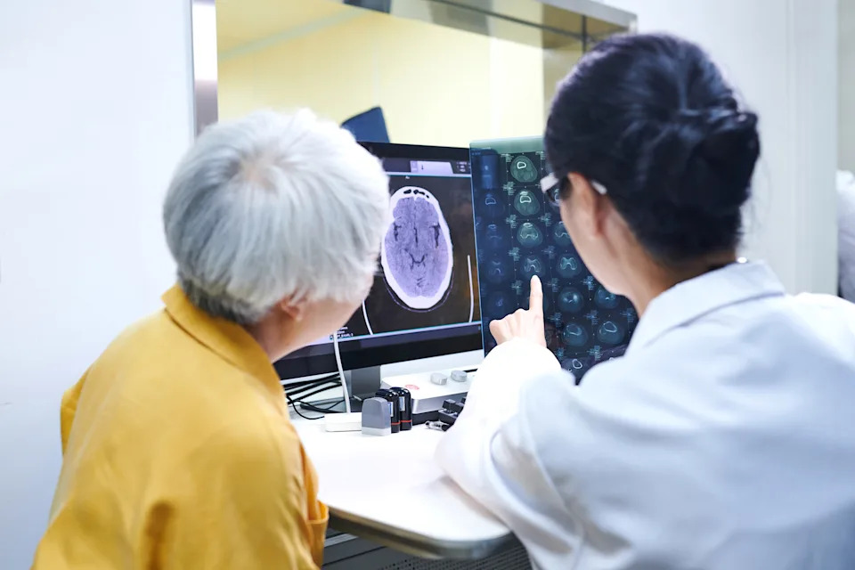 Rear view of asia doctor and senior female patient discussing solution while checking MRI film.