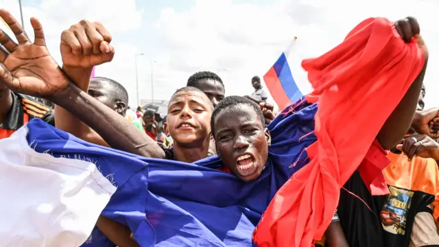 Man wey use Russian flag cover imsef wave im arms and shout as supporters of Niger military leaders gada to demonstrate outside di Niger and French airbase for Niamey, August 27, 2023
