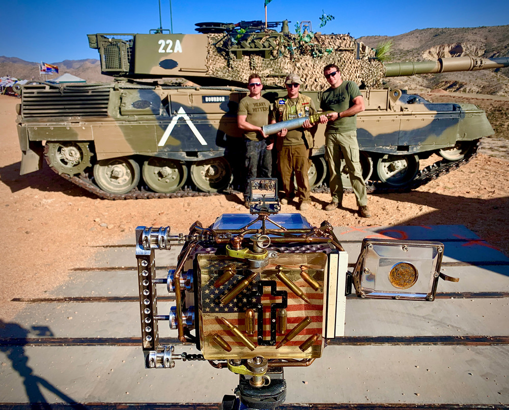 A Flock license plate reader behind a row of shrubs near the entrance of L.A. State Historic Park. A car drives past the park in the background.