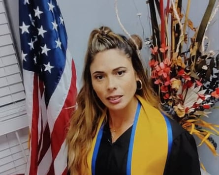 A young woman in a graduation gown in front of a US flag. 