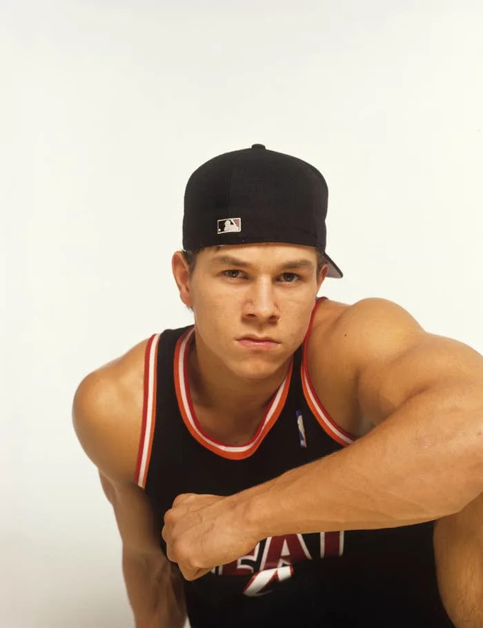 Mark Wahlberg in a casual sports tank top and cap, posing with a serious expression against a plain background