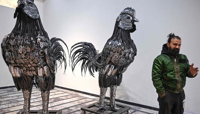 This photograph, taken on December 29, 2025, shows sculptor Ehtisham Jadoon standing next to rooster sculptures made from scrap metal at his studio on the outskirts of Islamabad. — AFP