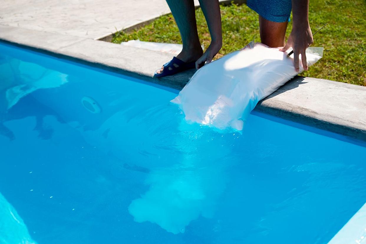 Stock image of someone putting a bag of disinfectant in a pool. Getty