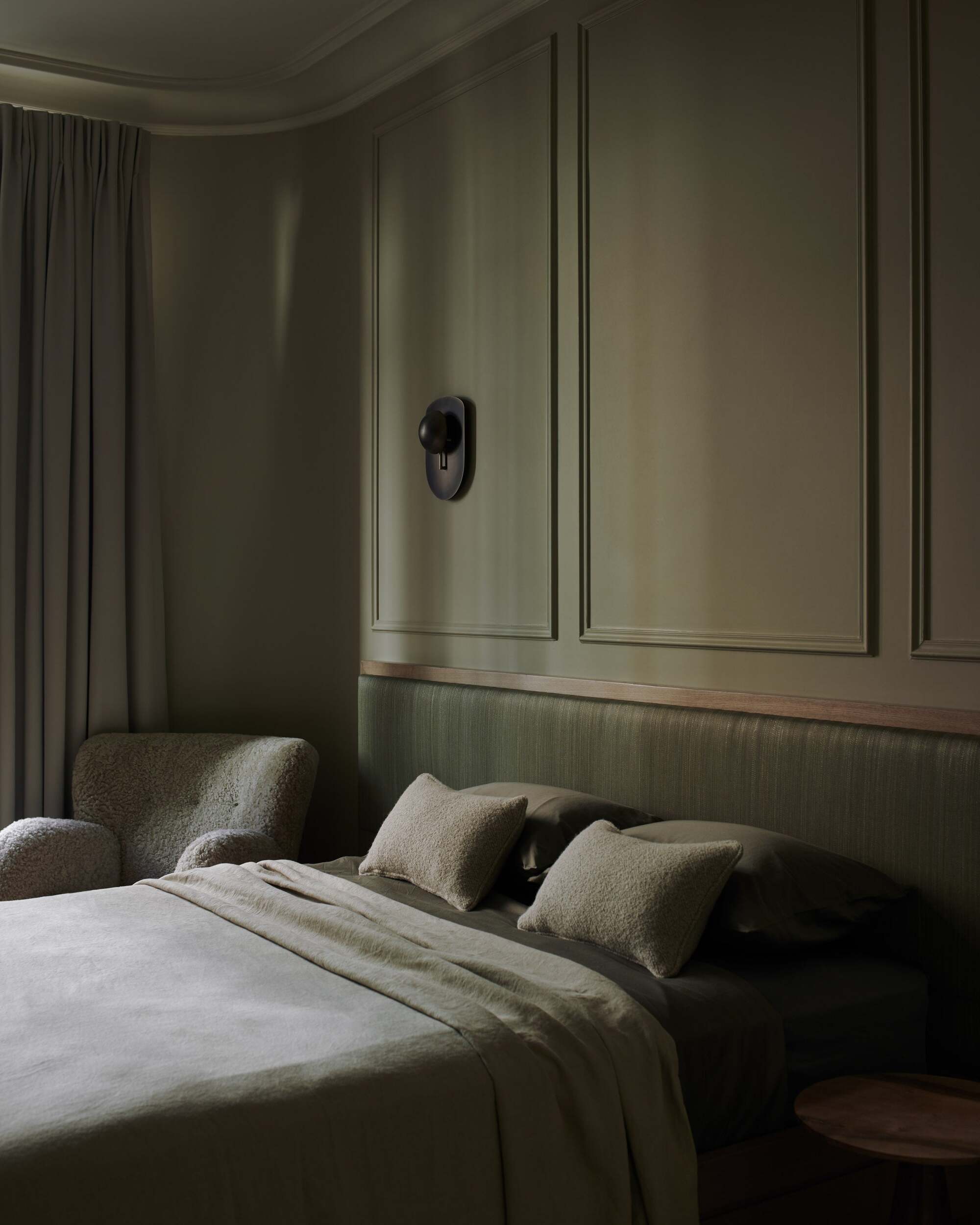 green color-drenched bedroom with wall moulding, green headboard, wall sconce, green bedding, boucle accent chair