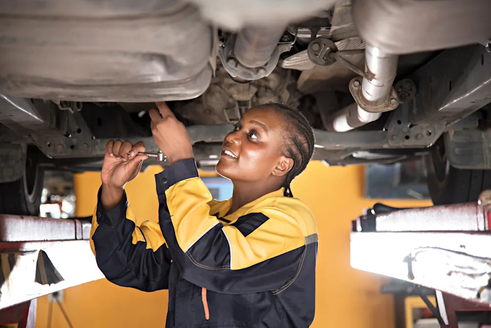 Mechanic in uniform works under a car on a lift, using a wrench, showcasing skilled labor in the automotive repair industry