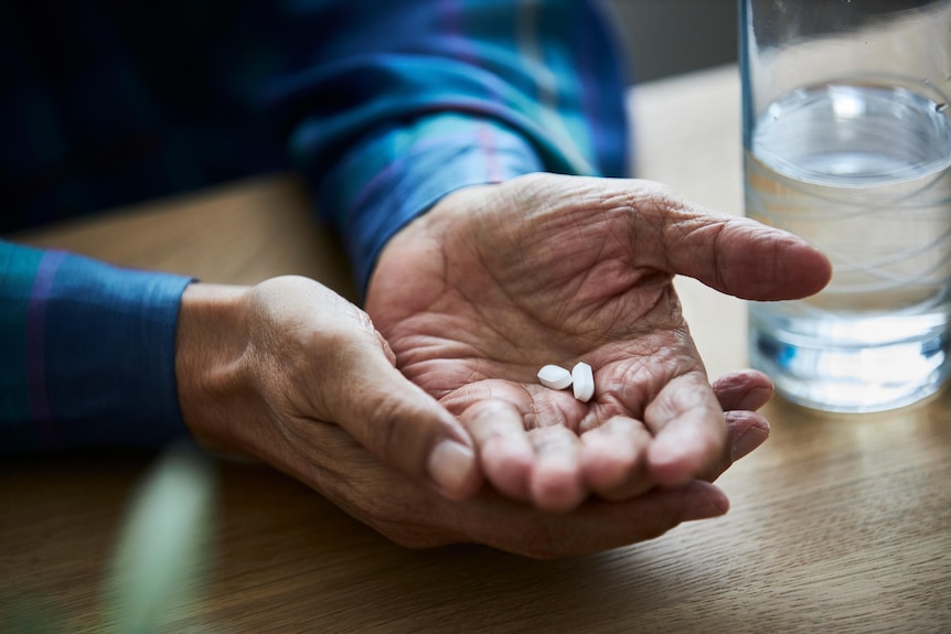 Close up of senior man holding pills in hand.