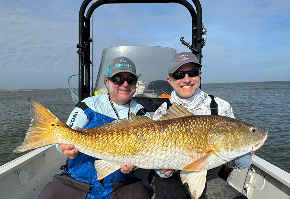 A Louisiana guide and a fisherman hold up a huge Louisiana redfish.