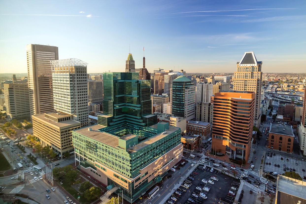 Aerial of downtown Baltimore, Maryland, buildings and cars on streets and parked in parking lots, sunlight coming through left side