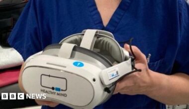 A woman in nursing scrubs holding a virtual reality headset