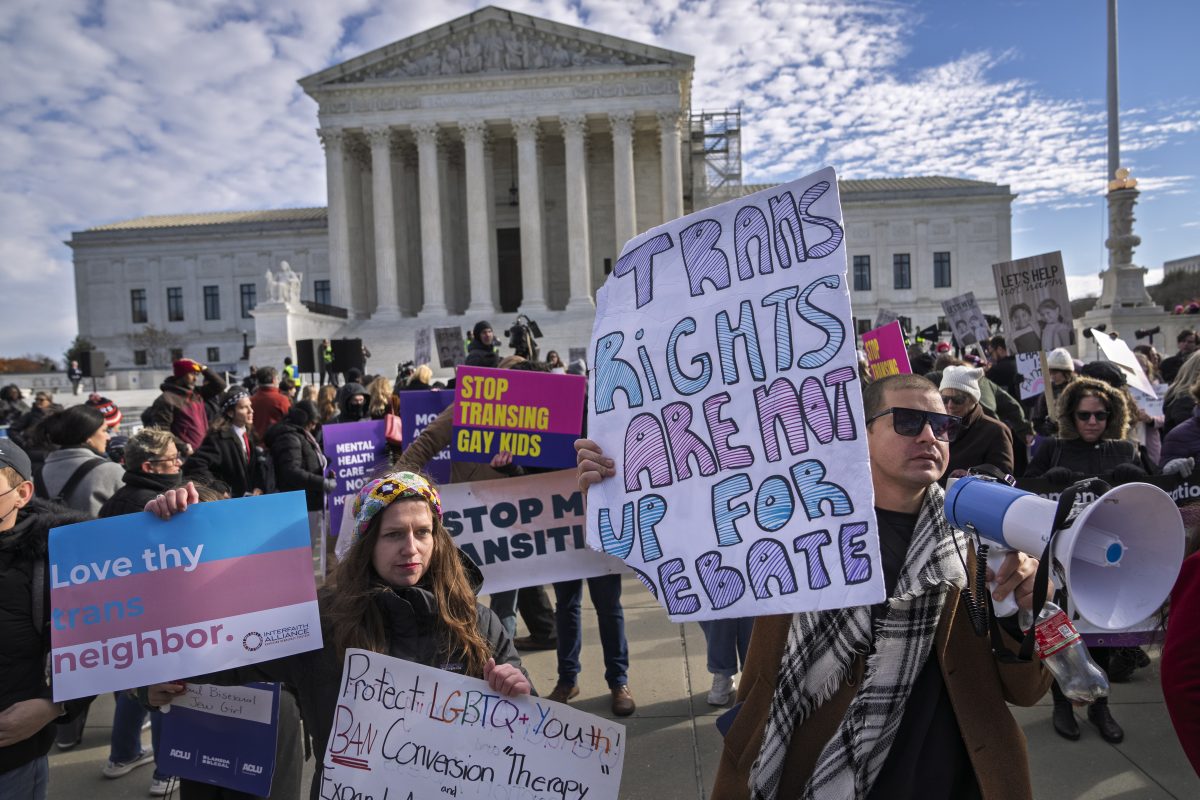 A group of people protest for transgender rights outside the U.S. Supreme Court, holding signs with messages supporting LGBTQ rights and opposition to conversion therapy.