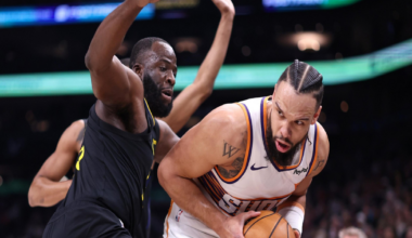 A basketball player in a white Suns uniform tightly clutches the ball while being closely guarded by a defender in a black Lakers uniform.