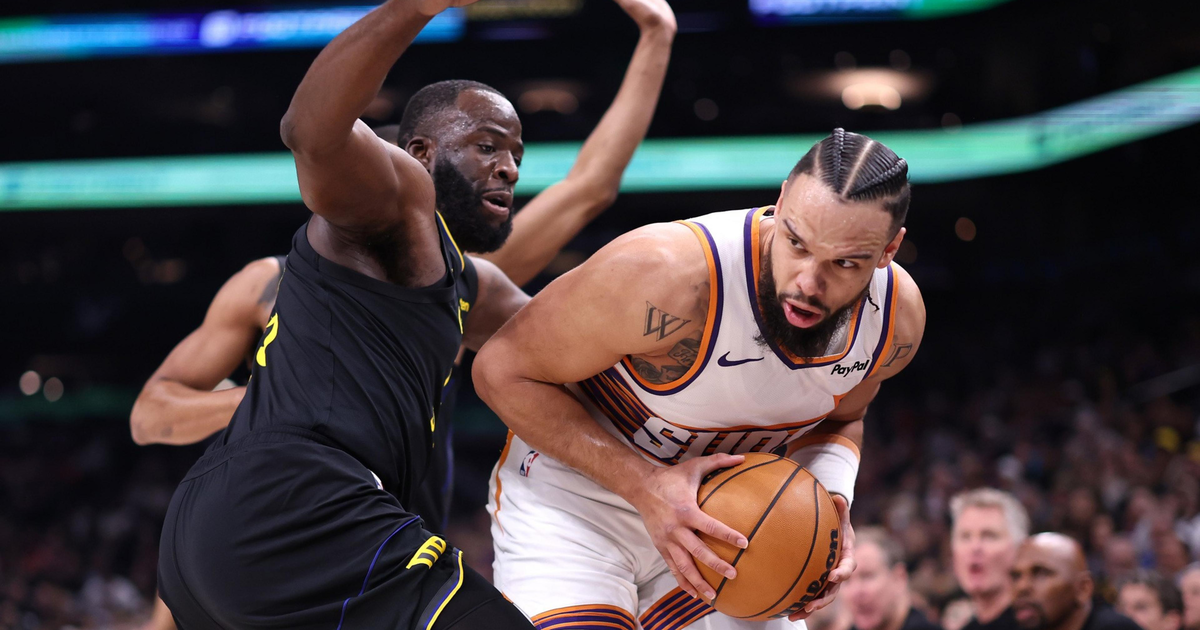 A basketball player in a white Suns uniform tightly clutches the ball while being closely guarded by a defender in a black Lakers uniform.