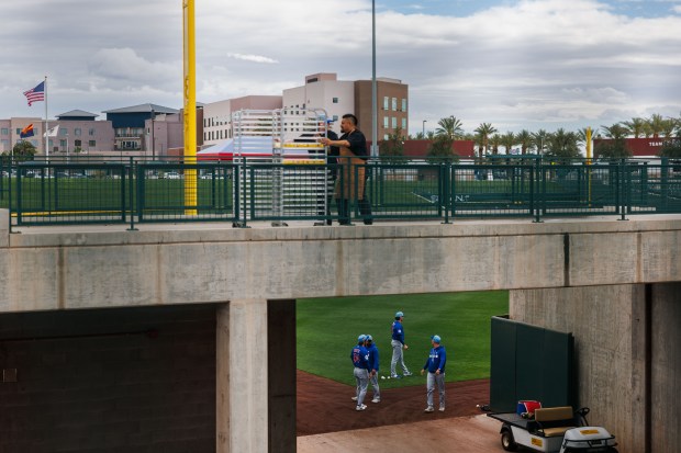 Cubs pitchers Riley Martin and Hunter Harvey walk on the field while workers move food over a bridge before live batting practice at spring training on Feb. 18, 2026, at Sloan Park in Mesa, Ariz. (Armando L. Sanchez/Chicago Tribune)