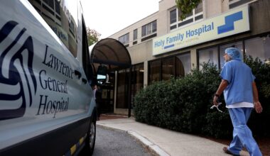 A staff member walks past a sign for Holy Family Hospital in Methuen, with a reference to Steward Health Care covered up following its takeover by Lawrence General Hospital, in 2024.
