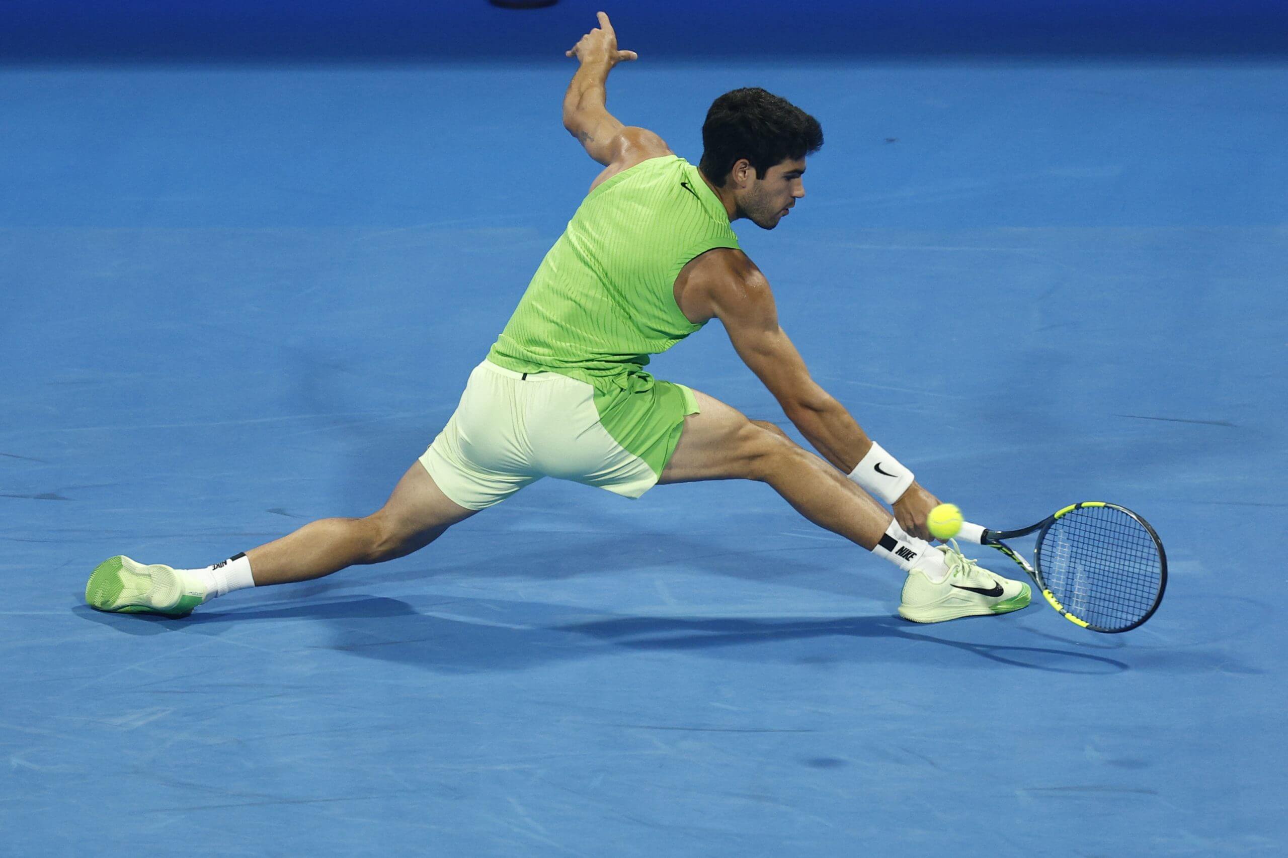 Carlos Alcaraz stretches to his left to hit a backhand slice on the slide with his back to the ball.
