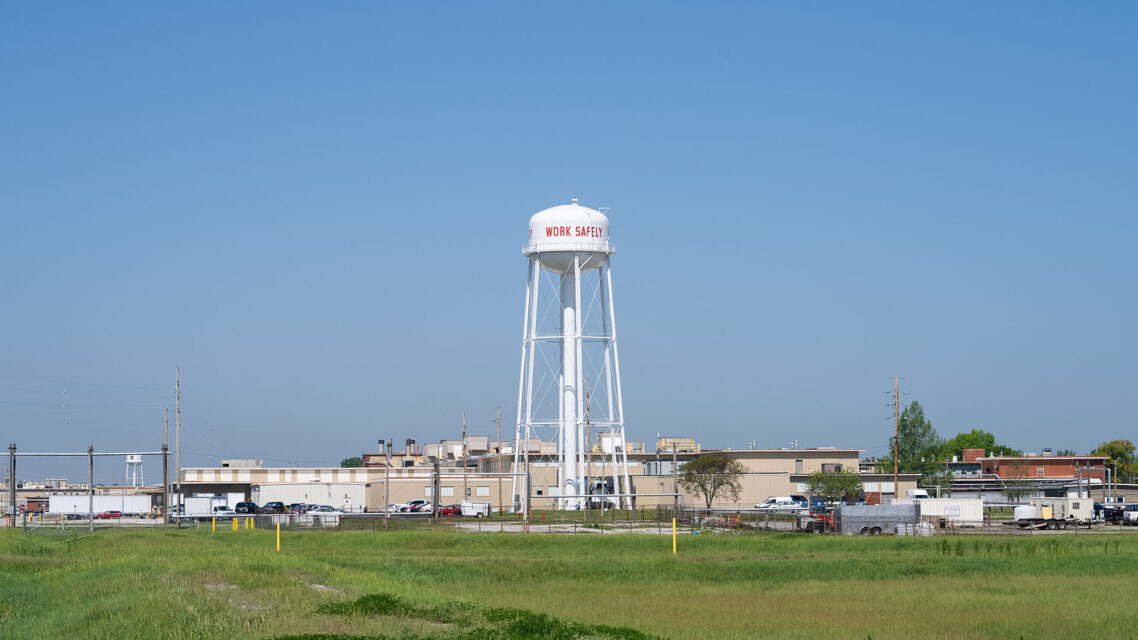Photo of a large white water tower with signage that reads 'Work safely' at the Lake City Army Ammunition Plant.