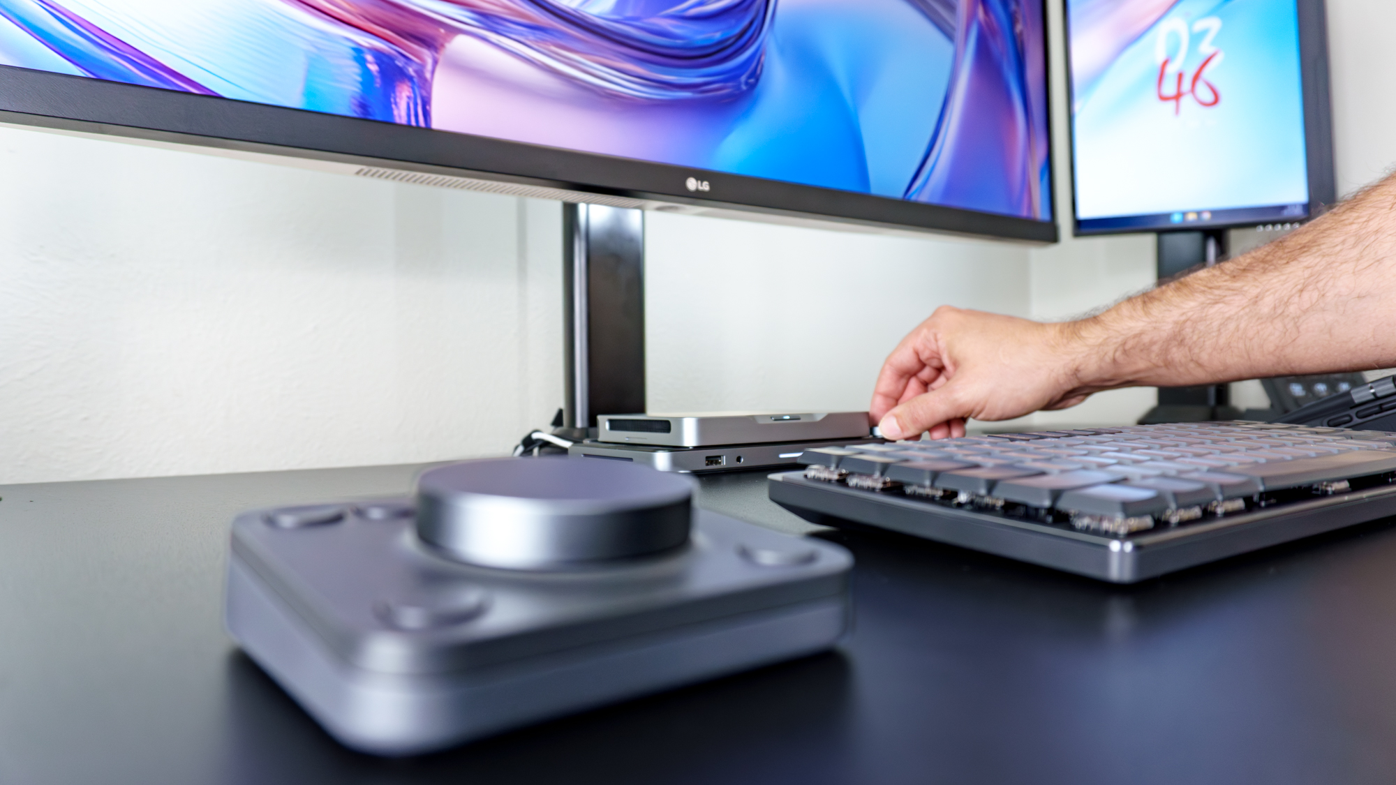 A person adjusting their computer's volume using the knob on the Mind Dock with Logitech's MX Dialpad next to its MX Mechanical Keys Mini keyboard in the foreground
