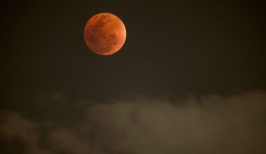 A red full moon is pictured above grey clouds in a dark night sky.