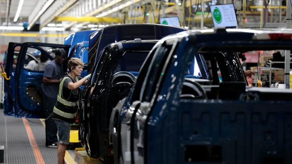 Workers on a car assembly line inspect partially assembled vehicles.