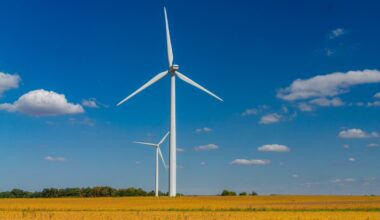 Two wind turbines stand against with a blue sky with cumulus clouds.