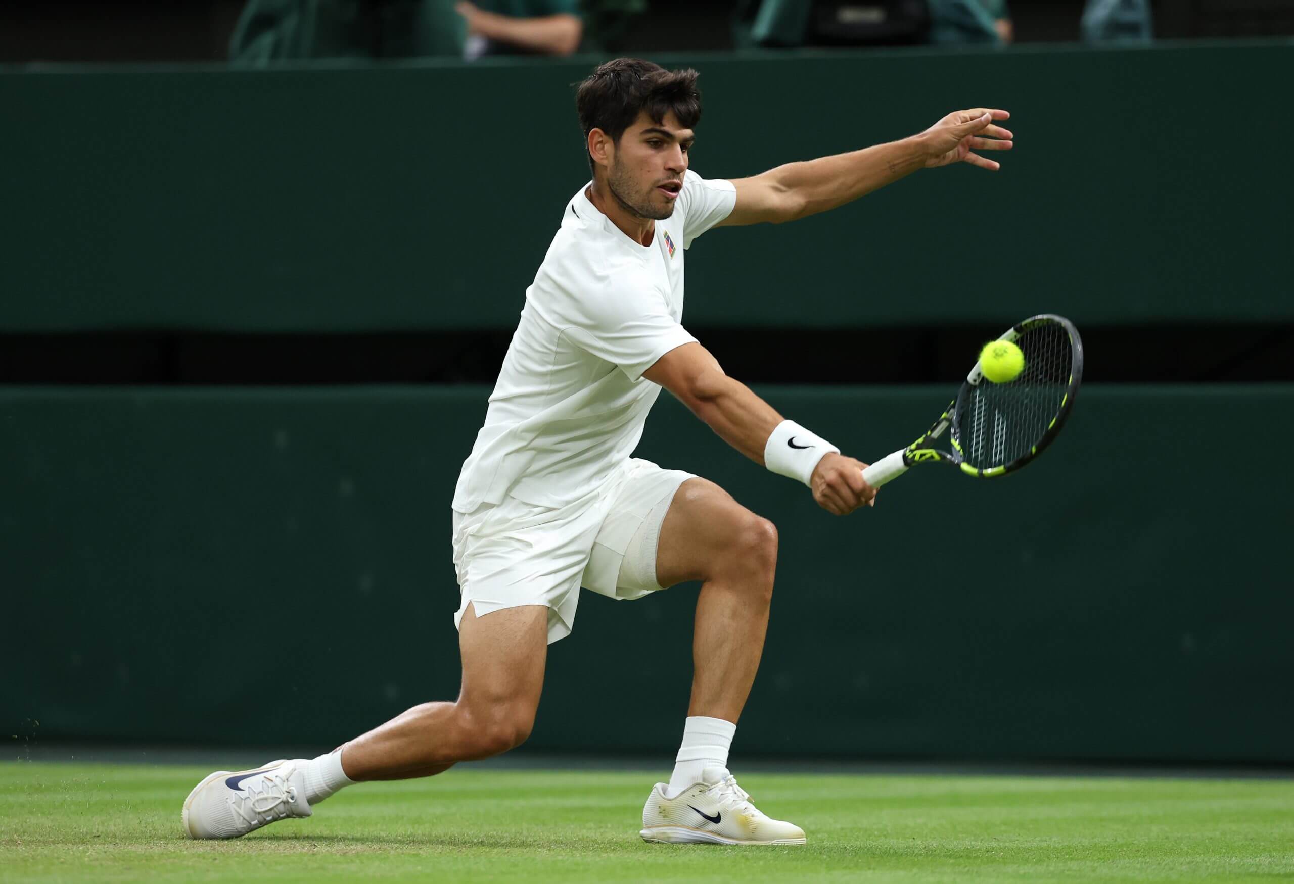 Carlos Alcaraz hits a backhand slice on a grass court with the tennis ball on his strings.