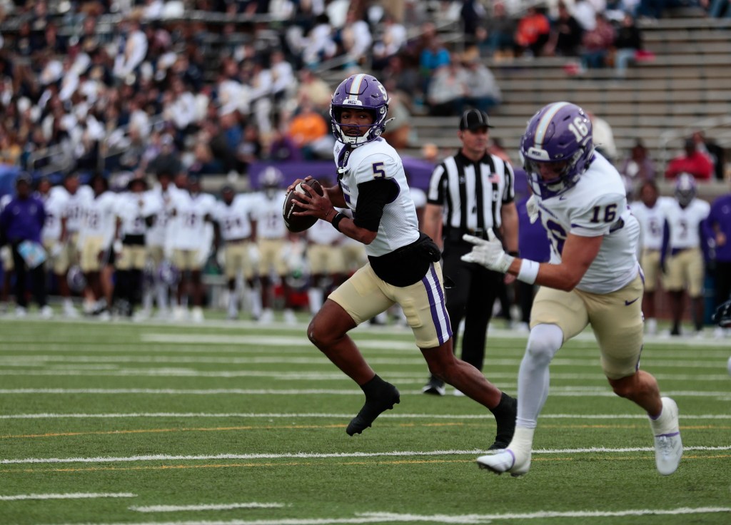 A Western Carolina football player in a purple helmet and white jersey with the number 5 runs with the ball on a green field.