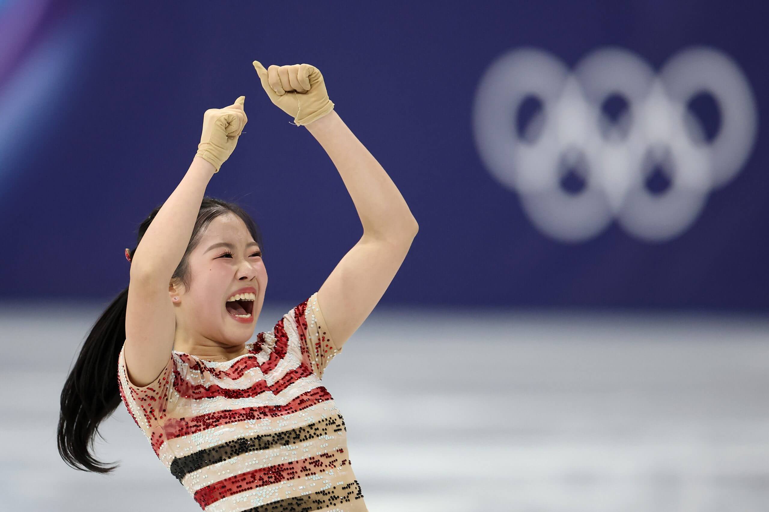 Ami Nakai, in an off-white sequined top with red and black stripes, holds her hands above her head in celebration, her fists clenched and her mouth open in a wide smile.