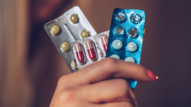 A hand holding three blister packs containing various tablets