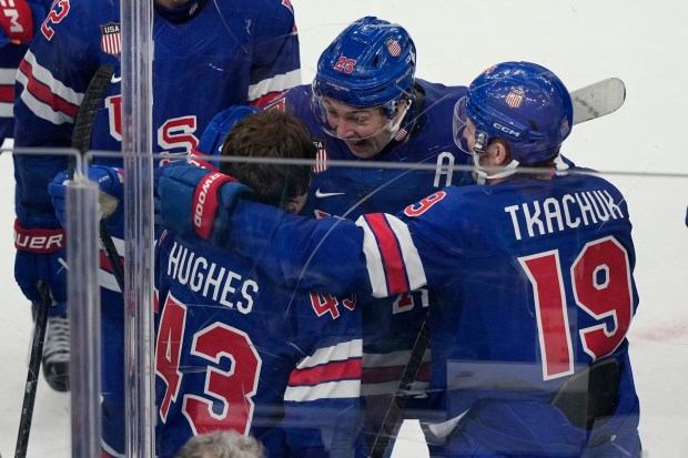 United States defenseman Charlie McAvoy, center, and Matthew Tkachuk (19) celebrate with Quinn Hughes, who scored the winning goal to beat Sweden in overtime in a men's ice hockey quarterfinal game at the 2026 Winter Olympics, in Milan, Italy, Wednesday, Feb. 18, 2026. (AP Photo/Hassan Ammar)