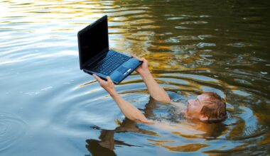A man submerged in water holding a laptop above the surface.