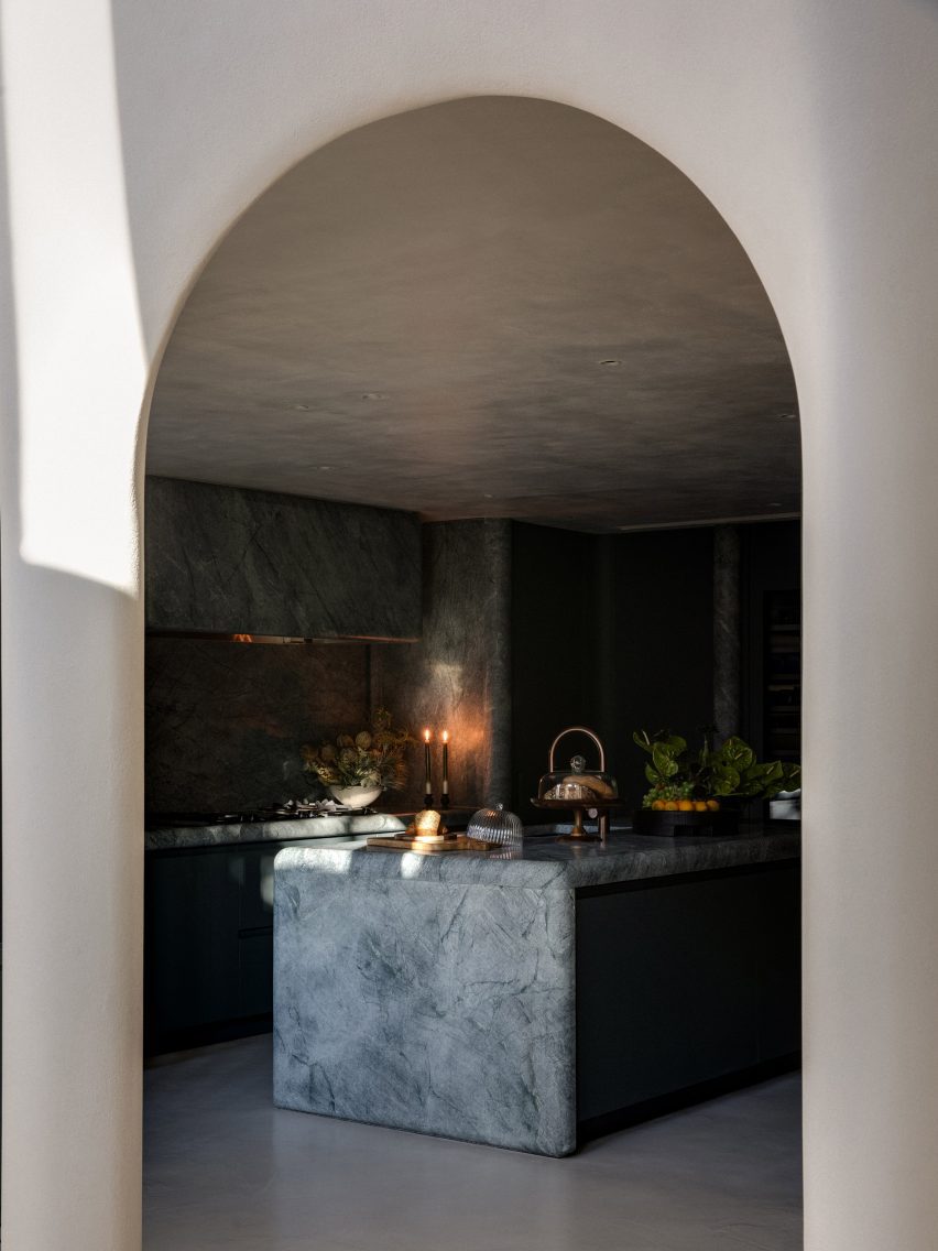 Through a tall white archway is the kitchen. A large marble island takes up the middle of the room.