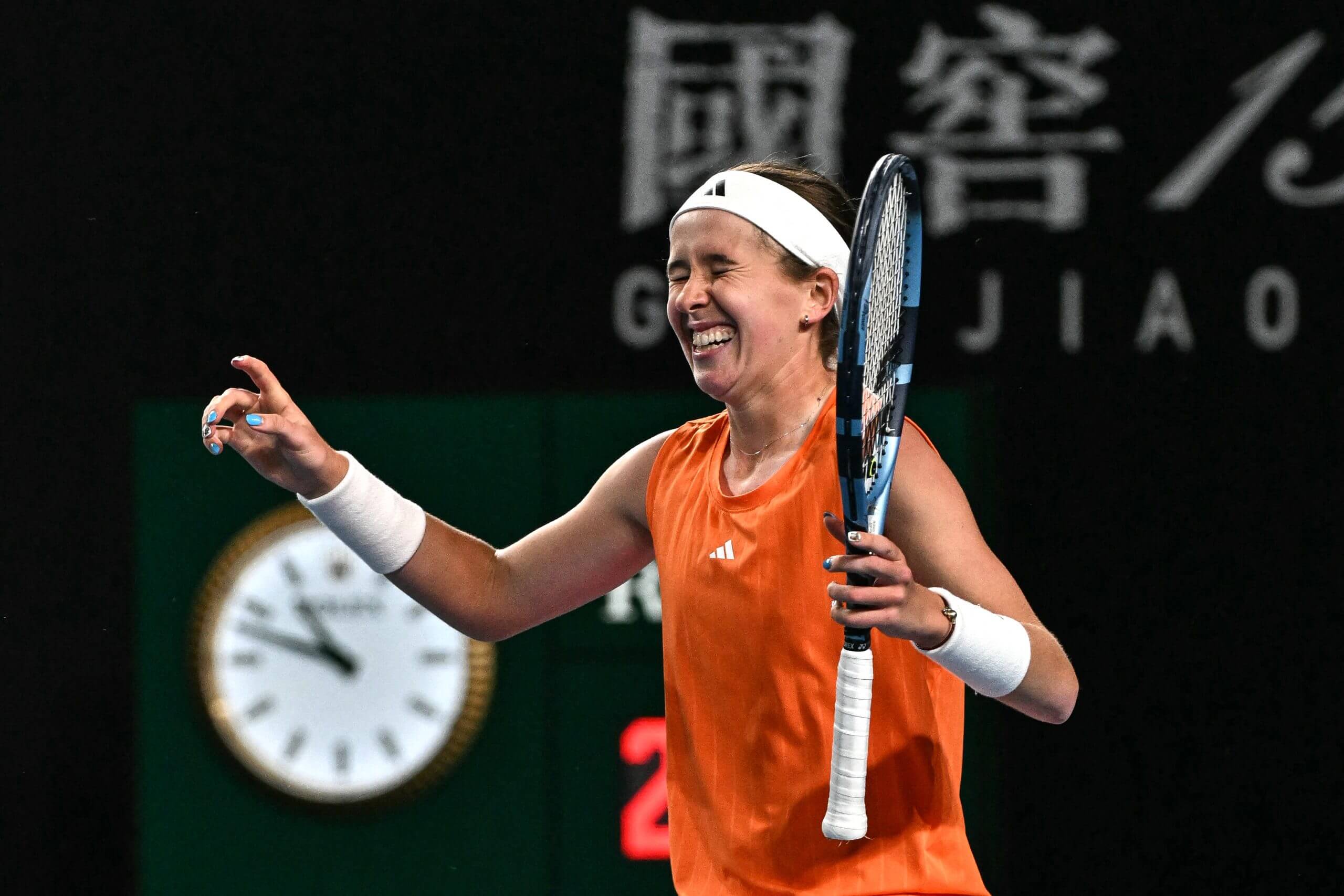 Nikola Bartůňková celebrates with her eyes closed and arms aloft wearing an orange tennis outfit.