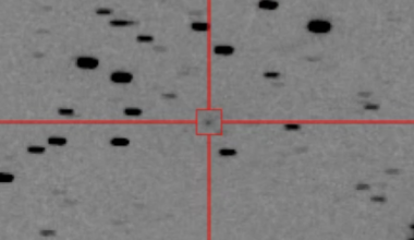 A black and white image shows a gray background speckled with dots with a crosshairs and a box circling a specific dot in the center of the image