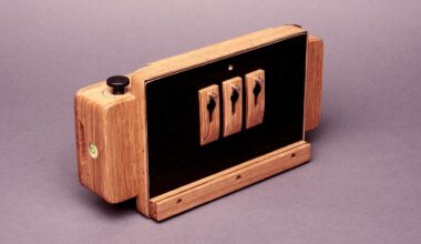 A handcrafted wooden camera with black panels and three toggle switches on the front, placed on a plain background. The design combines natural wood with functional hardware elements.