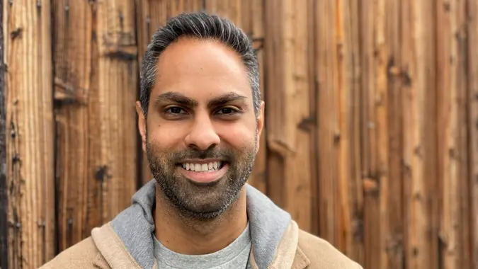Ramit Sethi smiling with a wooden wall in the background.