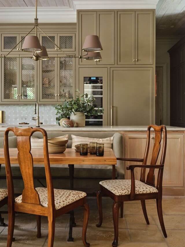 Claire Thompson's Interior Designs Are Soft, Warm, and Endlessly Livable - 5 A dining area with a wooden table, patterned chairs, glassware, and a built-in kitchen featuring beige cabinets and modern appliances—an inviting showcase of warm interiors by Claire Thompson.