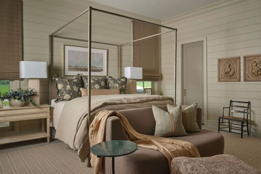 Claire Thompson's Interior Designs Are Soft, Warm, and Endlessly Livable - 10 A neatly arranged bedroom with a canopy bed, earth-toned bedding, and a small sofa at the foot blends warm interiors by Claire Thompson with textured interiors, side tables, and wall art—all in neutral, natural colors.