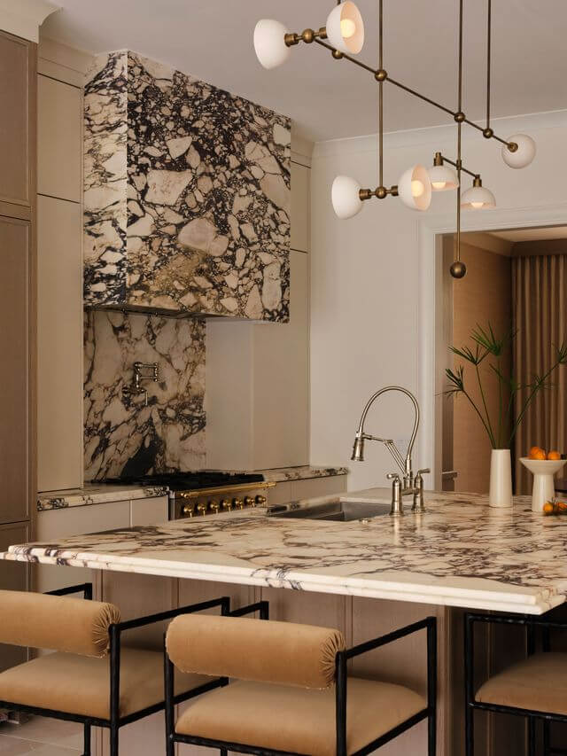 Claire Thompson's Interior Designs Are Soft, Warm, and Endlessly Livable - 11 Modern kitchen by Claire Thompson featuring a large marble island, matching textured marble backsplash and range hood, gold fixtures, beige barstools, and a contemporary chandelier for inviting, warm interiors.