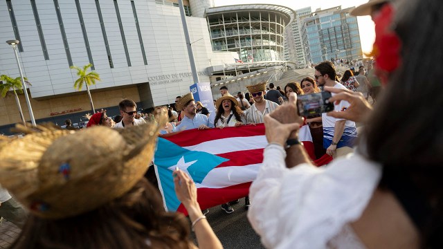 Photo showing people holding a Puerto Rican flag outside the Coliseo de Puerto Rico before singer and rapper Bad Bunny performs his first of 30 concerts at the arena in San Juan, Puerto Rico, on July 11, 2025.